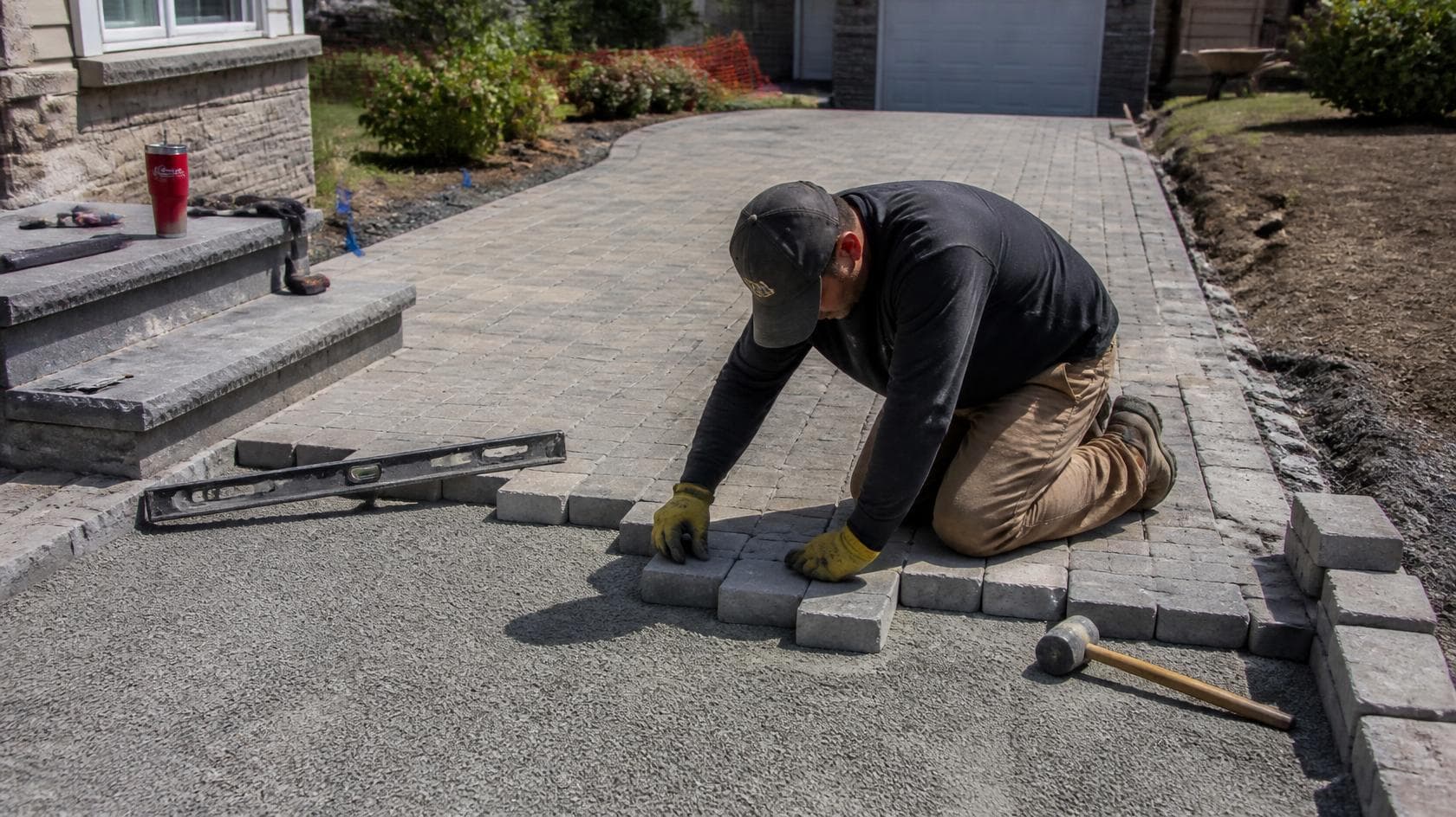 A landscaping crew in safety vests lowering a heavy stone block while building a retaining wall - Fieldwork Insurance
